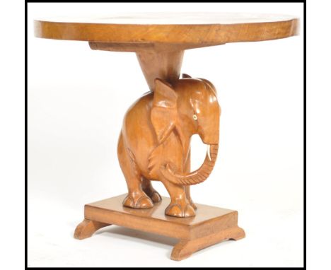 A mid century African hardwood lamp / side table having an oval solid table top supported by a carved elephant to the undersi