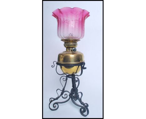 An early 20th century brass and cranberry glass shade oil lamp. Raised on a wrought metal rococo base with brass reservoir an