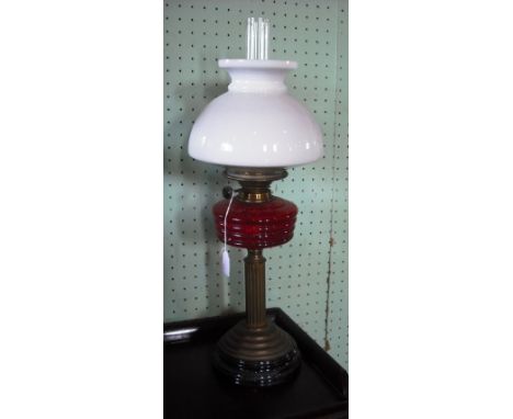 A brass column oil lamp with glass shade and cranberry reservoir.