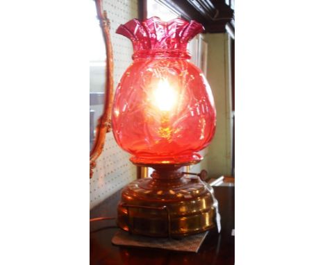 An Edwardian oil lamp, having a brass base and cranberry glass shade, now converted for electricity.