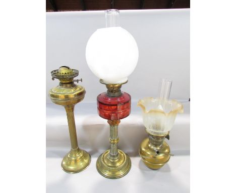 A Victorian brass column oil lamp with a cracked cranberry red font and an opaque shade, together with a converted brass oil 