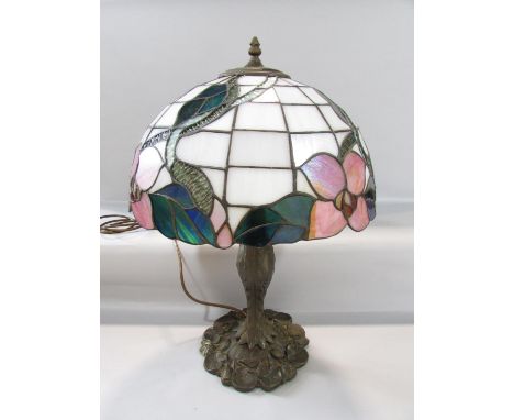 A Tiffany style table lamp with a floral “leaded” shade on a naturalistic bronzed base. 