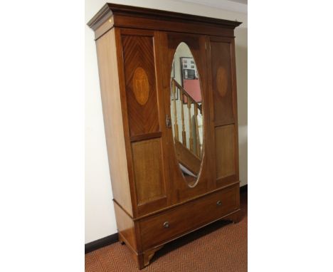 An Edwardian mahogany single door wardrobe, the overhanging cornice with a boxwood stringing raised above an oval mirror flan