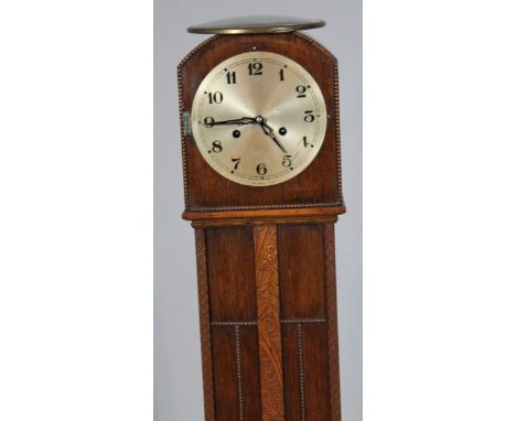 A 1920's oak granddaughter clock, with 16cm dia. Arabic dial in a carved case revealing an eight day movement, the whole rais
