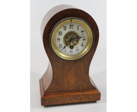 An Edwardian oak cased balloon mantel clock, with raised 9cm dia. Arabic dial with fancy floral centre and shaped pointers, i