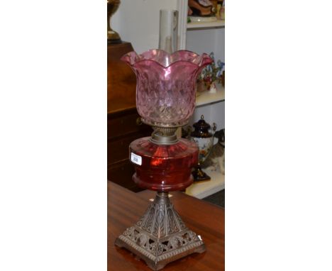An Edwardian wrought iron and cranberry glass oil lamp