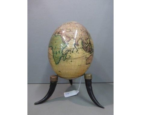 An ostrich egg decorated with maps of the world, displayed upon a tripod base. 