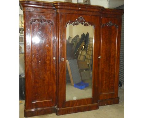 A mid Victorian figured mahogany triple wardrobe with hanging compartment, trays and drawers enclosed by a large central mirr