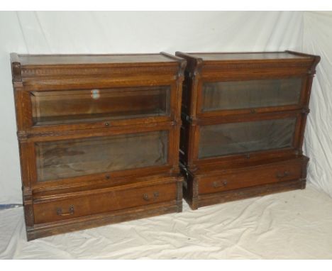 A pair of oak stacking bookcases by Globe Wernicke, each with two compartments enclosed by bevelled glazed folding fronts abo