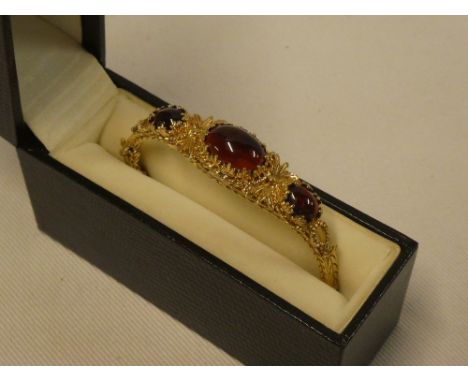 An ornate 9ct gold oval bangle mounted with three cabochon garnets