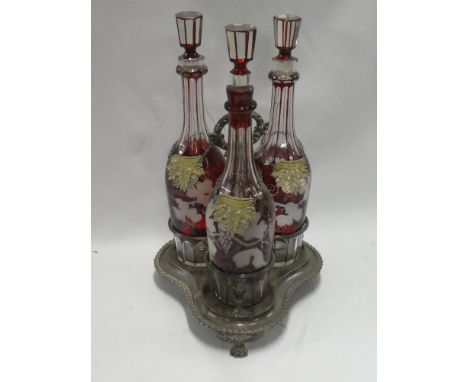 A set of Bohemian-style cut glass ruby tinted decanters and stoppers with vine leaf decoration on silver-plated trefoil stand