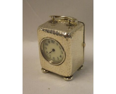 A small silver cased travelling clock with circular enamelled dial in beaten rectangular case