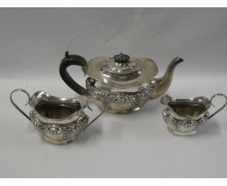 An Edward VII silver oval three-piece tea set comprising teapot with hinged lid, raised scroll decoration and ebonised handle