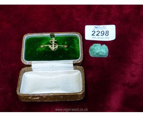 A Gold anchor pin and a small green jade animal.