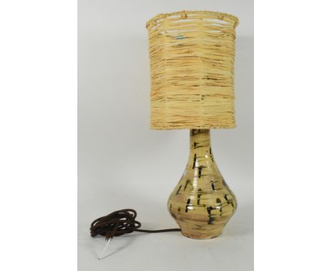 A 20th century monochrome studio pottery table lamp. The lamp having raffia shade of cylindrical form over a pottery base wit