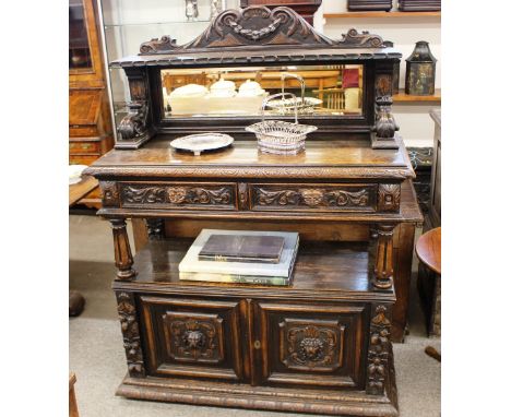 A Victorian carved oak two tier buffet, the top surmounted by a mirrored shelf, raised on scrolled supports, two drawers belo