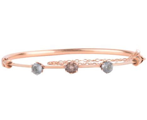 An Early 20th-century gem-set hinged bracelet, composed of a knife-edge band mounted with topaz and two blue zircons in coron