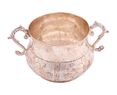 A Charles II silver two-handled porringer, the body decorated with four panels of flowerheads, twin cast S scroll handles and