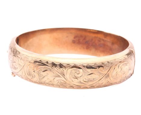 A 9ct yellow gold hinged bangle, half of the hollow bracelet is engraved with bright-cut scrollwork patterns, completed with 