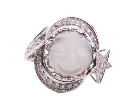 A carved moonstone and diamond dress ring, depicting a smiling face on the round moonstone cabochon, in a surround stylised a