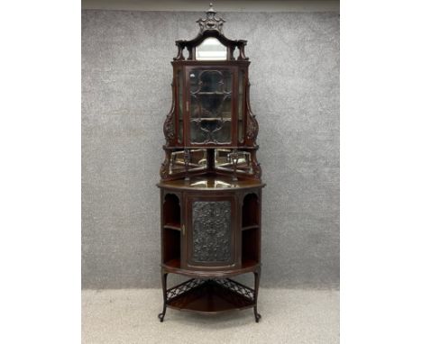 An Edwardian mahogany corner cabinet in two parts having a carved cresting above a shaped pediment inset with a bevelled mirr