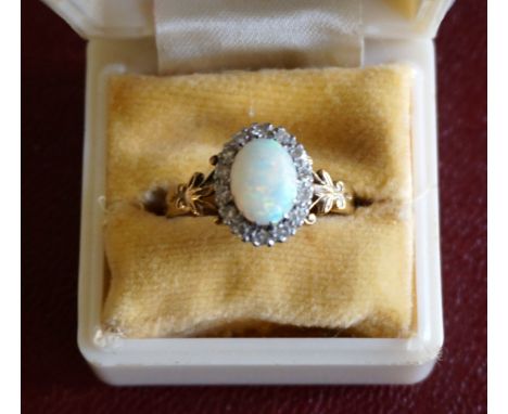 A late Victorian/Edwardian 18ct yellow gold and platinum ring, set with a central oval opal amidst an outer ring of diamonds.