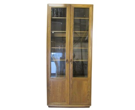 A Ercol elm upright bookcase, enclosed by a pair of full length doors, three quarter glazed, with adjustable shelves, 215cm h