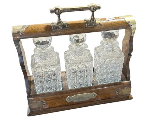An Edwardian oak and silver plated three bottle tantalus with hinged fall front panel with lock and key. 