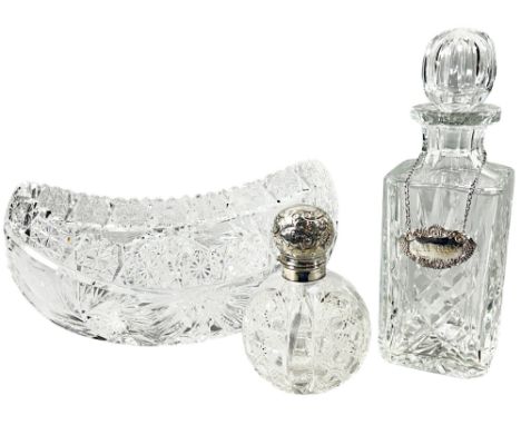 A boat shaped cut glass fruit bowl, a square cut glass decanter, and a perfume bottle with a silver cap.