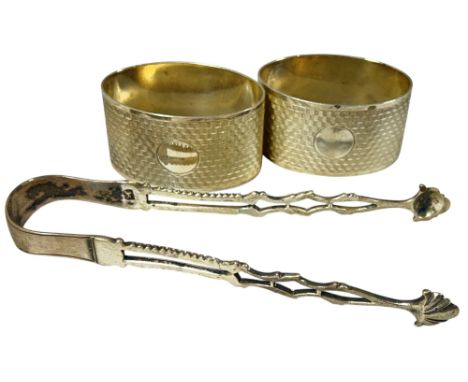 A pair of engine turned silver napkin rings and a pair sugar tongs, 2.9 oz