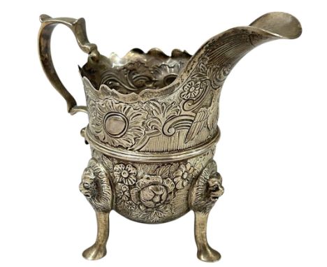 A Victorian silver cream jug in the Irish manner, London 1899, helmet shaped, profusely chased with birds scrolls and flowerh