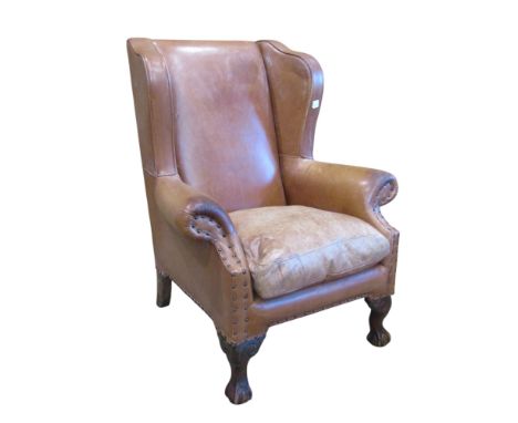 A Georgian style tan leather upholstered wing armchair on claw and ball supports 