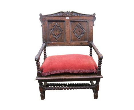 An antique oak elbow chair of wide proportions, with panelled back and bobbin supports
