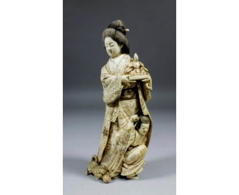 A Japanese carved ivory okimono of a Geisha holding a model of a seated male figure with a young child by her feet playing wi