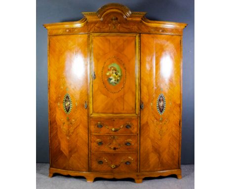 An Edwardian satinwood and painted bow-front wardrobe of Neo-classical design with matched veneer panels and painted with a b