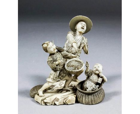 A Japanese carved ivory okimono in the form of a standing fisherman and child holding a basket with a fish and another child 