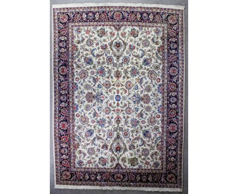 A Mashad carpet woven in colours with bold floral palmettes and trailing leaf ornament within an ivory ground within floral f