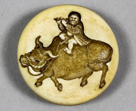 A Japanese carved ivory circular toggle, the face carved and stained with a child playing a flute astride a buffalo, the reve