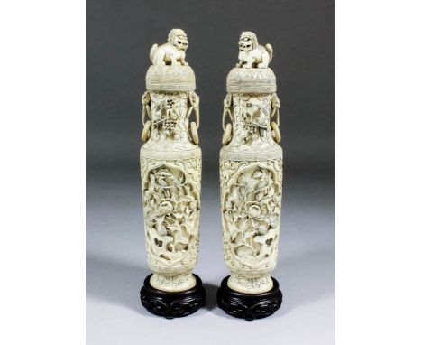 A pair of Chinese "Cantonese" ivory oval section two handled vases and covers, the bodies finely carved with shaped vignettes