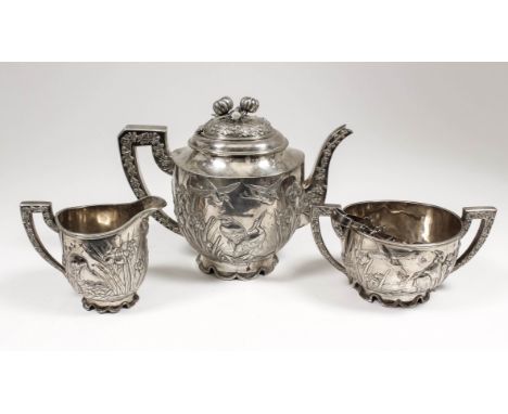 A Chinese cast silver three piece tea service, the oval bodies cast with cranes underneath bulrushes and irises, with spout a