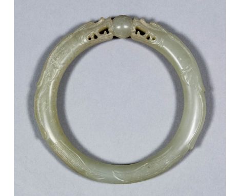 A Chinese pale celadon jade bangle carved with two dragons heads supporting a ball, 3ins (76mm) diameter