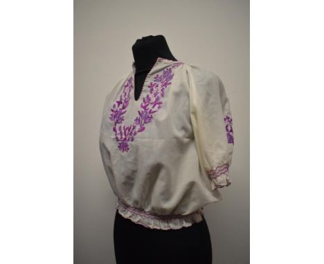 A vintage peasant blouse, having purple hued embroidery, smocking to sleeves and hem and press stud fastening to waist.