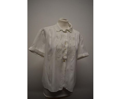 A white 1950s blouse having machine embroidered floral decoration, shaped collar, buttons to front and turn up cuffs.