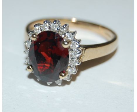 A modern 9ct gold four claw oval cut garnet set dress ring in a surround of small brilliant cut diamonds