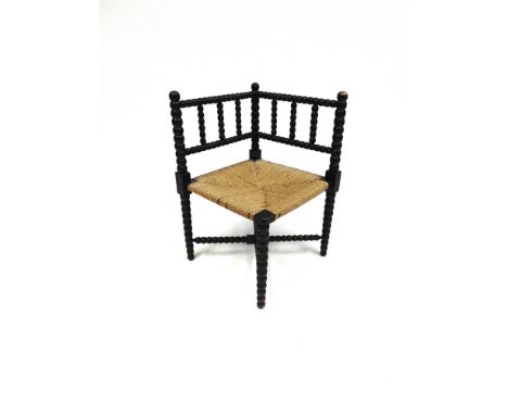 AN EBONISED BOBBIN FRAMED CORNER CHAIR with rush seat and cross stretcher under, 39cm square, 62cm high