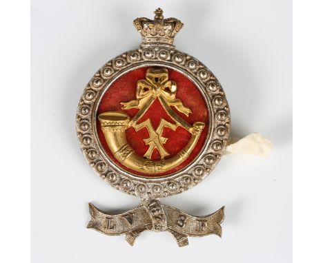 An unusual Victorian silvered metal helmet plate badge with crown above a gilt slung bugle over a red fabric backing and lowe