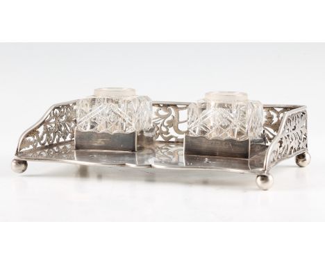 A silver double inkwell stand with cut glass inkwells (no lids), the stand featuring pierced sides and raised on four ball fe