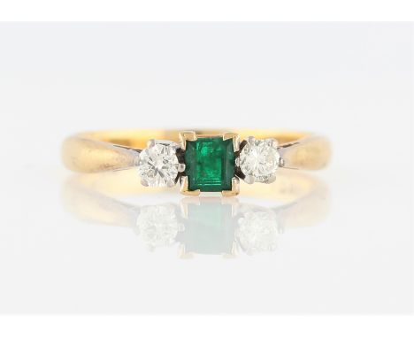 An emerald and diamond three stone ring, set with a central square cut emerald, measuring approx. 3x3mm, flanked to either si