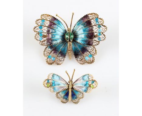 Two filigree butterfly brooches, each having purple and blue enamel to body, one being slightly larger than the other, both s