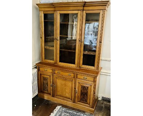 An Art Nouveau light oak bookcase, in an , moulded cornice in a breakfront shape, above three glazed cabinets enclosing adjus